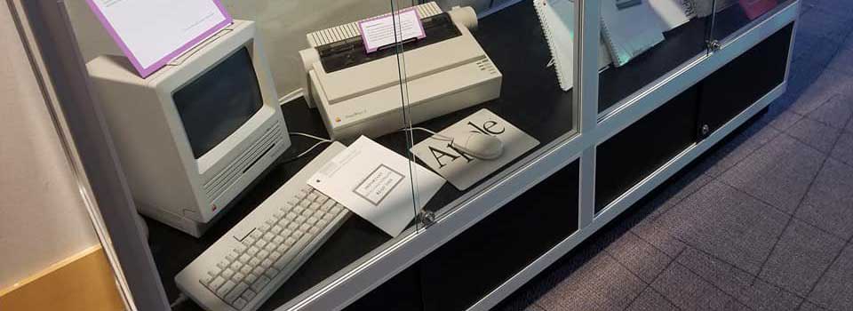 An old macintosh computer, mouse, keyboard, and printer in a display case at the MGA museum of technology