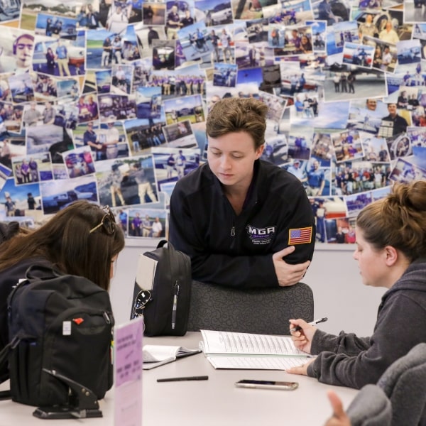 Students peering over a table at Aviation hall, a collage of Eastman campus students decorate the wall behind them