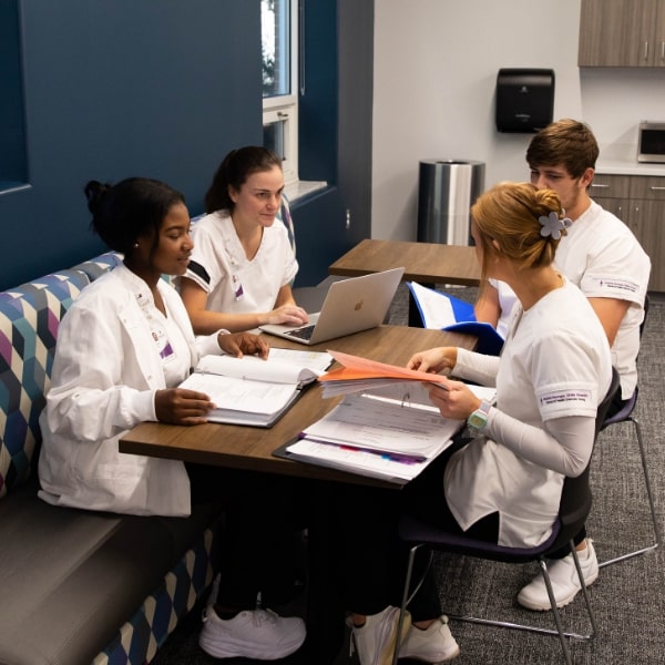 Four nursing students seated together, studying with their textbooks open in front of them