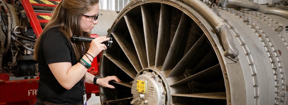 A woman with a flashlight inspects a jet engine