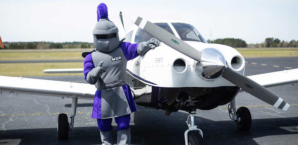 University Knight mascot standing next to a small propeller airplane  