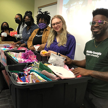 A group of smiling people around bins filled with donation supplies