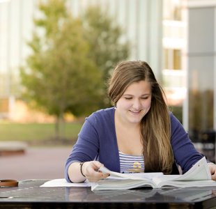 Woman at a table outdoors looking through a book.