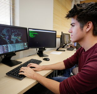 Students behind computer desks in a classroom, looking at professor.